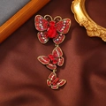 Detail of a vintage butterfly brooch featuring red rhinestones on dark silk fabric - Red