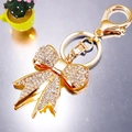 Golden metal bow keychain with shimmering rhinestones and clasp on reflective surface - Full Rhinestone Bowknot White / White