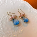 Vue macro des boucles d'oreilles zircon bleu avec fleurs colorées sur céramique blanche - Bleu