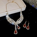 Dettaglio del set di gioielli con pietre rosse a goccia e strass scintillanti su vassoio - Oro-Rosso