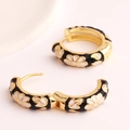 Detail of golden hoop earrings with black enamel and white daisy floral patterns - Black