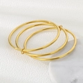 Detailansicht von drei ineinandergreifenden 3mm Gold-Edelstahl-Armreifen auf Stoff - 55mm / Dreifachringe (Vollgold)