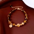 Vista macro del bracciale di perle occhio di tigre placcato oro 18k su velluto rosso - Stile Ciondolo Moneta (Caffè-Oro)