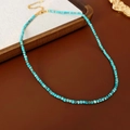 Detail of blue turquoise beaded necklace featuring a gold metal clasp on a wooden tray - Gold-Blue