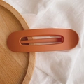 Detailed view of matte caramel duckbill hair clip on elegant wooden and fabric textures - Matte Bright Orange