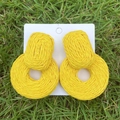Detailed view of yellow woven raffia earrings on natural green grass background - Bright Yellow Geometric Round Woven Earrings