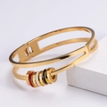 Close-up of double-layered gold plated bangle featuring tricolor enamel ring charms - Gold