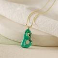 Close-up of green enamel letter pendant with gold-plated chain on white fabric - Letter B