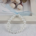 Detailed view of girls' white pearl bracelet with a blue ribbon bow on wooden background - 8MM Cream White Pearl With Blue Ribbon Bracelet