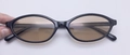 Detailansicht der ovalen schwarzen Fassung und braunen Gläser der Retro-Sonnenbrille - Schwarzer Rahmen Champagner Linsen