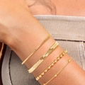 Detail of layered gold Figaro, snake and bead chain bracelets on a female wrist - SL173 Gold