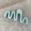 Detail showing wave-shaped blue hair claw clip with glossy jelly finish on textured paper - Tiffany Blue