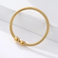 Macro detail of golden twisted cable bangle with smooth spherical ends on white podium - Gold