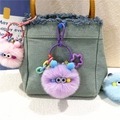 Cute plush monster keychain with colorful beads hanging on a denim bag strap - Purple
