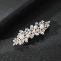 Macro shot of leaf-shaped hair clip with sparkling rhinestones and white pearls on black leather - Pearl Style / Gold