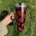 40oz black stainless steel tumbler with red disco heart patterns held outdoors over grass - A1 / Red Disco Heart