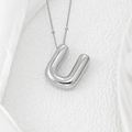 Macro shot of silver balloon letter U pendant on a ball chain over white silk - Letter U Pendant