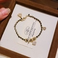 Dettaglio del bracciale in pelle intrecciata nera e catena d'oro con trifogli e zirconi - Oro Nero