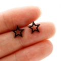 Black cutout star studs in stainless steel, minimalist design shown on fingertip - Black