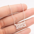 Detailed macro of silver gothic 1985 year pendant necklace held by fingers - 1985 / Steel