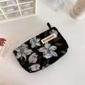 Detail of floral relief pouch with black base and white flower prints on a white table - Black Flower
