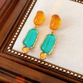 Close-up of vintage resin earrings with orange and cyan translucent stones in gold frames - Yellow-Blue