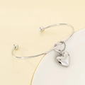Detalle del brazalete de nudo plateado con un colgante de corazón pulido en superficie lisa - Color Acero