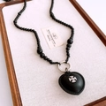 Detailed macro view of black beaded necklace with leather heart pendant and metal cross icon - Necklace-Black-Heart