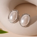 Close-up of vintage oval pearl earrings with irregular silver borders on a ceramic base - Silver Oval Pearl Stud Earrings / Silver
