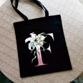 Black canvas tote bag featuring a pink letter F and white lily floral print - Letter F / Black