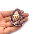 Waterdrop shell pendant with pink resin stone and rhinestones held in hand - Dark Red