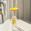 Close-up of glass tumbler with lemon graphics, yellow lid, and glass straw on table - Lemon + Lid + Straw