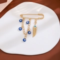 Gold evil eye brooch with blue charms and feather tassel on a minimalist display - Feather Evil Eye Style (Z345)