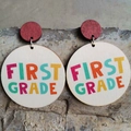Bunte First Grade Holzohrringe mit roten runden Steckern auf Betonhintergrund - Erste Klasse