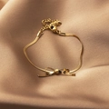 Bracelet doré avec élément nœud et chaîne serpent sur fond de satin champagne - Bracelet Or