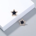 Detailed close-up of gold-plated star earrings with black enamel and white zircon inlay - Star Studs / Black & Gold