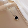 Detail van zilveren boxketting met zwarte ronde hanger op witte zijde en gouden dienblad - Zilver