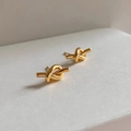 Close-up of golden knotted stud earrings featuring a high-polish metallic finish - Knot / Gold