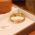 Detail eines goldenen Edelstahl-Mesh-Armbands mit Herz- und Buchstaben-A-Anhänger - Buchstabe A