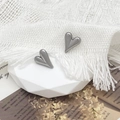 Detailed view of silver heart earrings on a white geometric stand with fabric background - Steel