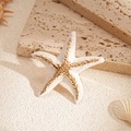 Detail eines weißen Seestern-Rings mit Goldrand auf Naturstein und Sandhintergrund - Weißer Seestern-Stil