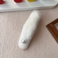 Dettaglio di un fermaglio per capelli in peluche bianco con perla su sfondo beige - Stile Perla / Bianco