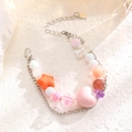 Primer plano de pulsera de cuentas macaron con dijes de corazón rosa y placa CONER - Cuentas Macaron Rosa Naranja