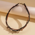 Détail d'un ras-de-cou en cuir vintage avec anneaux en bronze sur un support neutre - Style Épissé Papillon Noir