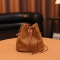 Brown minimalist drawstring bucket bag with metal ring detail on a wooden table - Brown