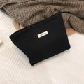 Close-up detail of black woven tweed cosmetic bag with simple wish label on bedding - Black