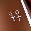 Dettaglio macro di orecchini a croce in argento con zirconi bianchi su sfondo strutturato - Fibbia per Orecchio - Stile Croce Con Zirconi Completi Argento