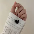 Detail einer silbernen Büroklammerkette mit schwarzem Herzanhänger in der Hand - Schwarze Glaskette