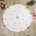 White Christmas tree skirt with red embroidery and colorful pom-poms on wood floor - Embroidered Tree Skirt / White