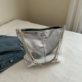 Silver metallic bucket bag with gold chain strap placed on white bedding decor - Silver